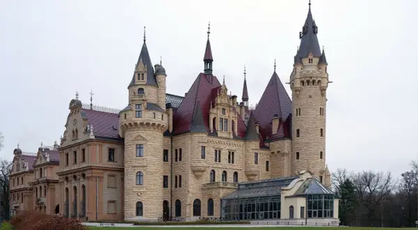 Zamek Książ, jeden z najpiękniejszych zamków w Polsce, z wieżami i czerwonymi dachami, otoczony zielenią.