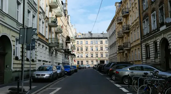 Ulica w kamienicach, typowa dla **południa Polski**. Samochody stoją zaparkowane wzdłuż chodnika, a na pierwszym planie widać rowery.