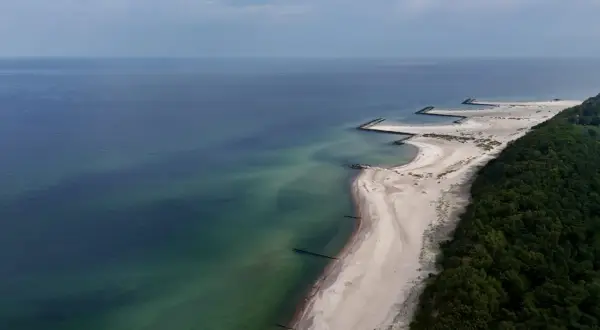 Widok z lotu ptaka na plażę w Jarosławcu z kamiennymi falochronami tworzącymi kształt przypominający molo.