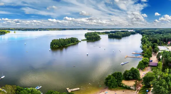 Malownicze zalewy w Polsce z żaglówkami, wyspami i plażą pełną wypoczywających ludzi.