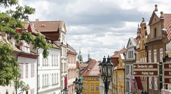 Ulica w Pradze z zabytkowymi kamienicami i latarniami. W oddali widać wieże, wskazujące na praga nietypowe atrakcje.