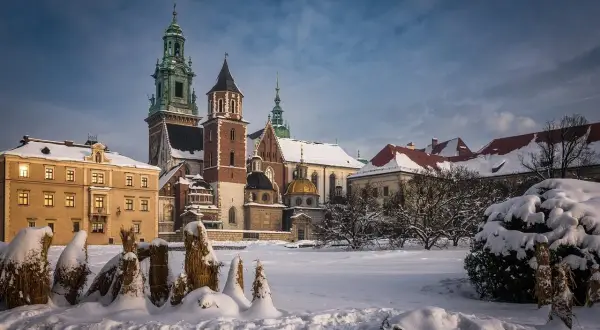 Zamek Królewski na Wawelu w zimowej scenerii. Pokryte śniegiem dachy i drzewa tworzą magiczny widok, idealny na kraków atrakcje zimą.