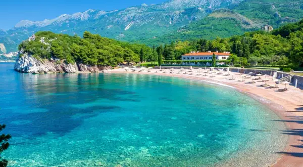 Malownicza zatoka z piaszczystymi plażami w Czarnogórze. Turkusowa woda, zielone wzgórza i biały budynek hotelu tworzą idylliczny krajobraz.