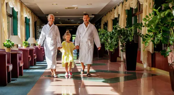 Rodzina w szlafrokach idzie korytarzem hotelowym. To idealne miejsce, by poczuć, co to jest spa i odpocząć.