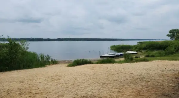 Piaszczysta plaża nad Zalewem Porajskim, z kilkoma łódkami przy brzegu. Idealne miejsce na wypoczynek i podziwianie przyrody.