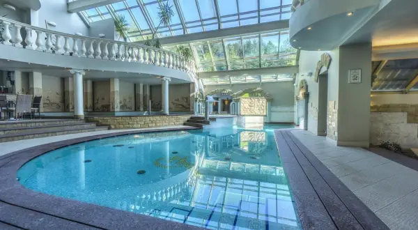 Basen w hotelu Szczyrk Klimczok z przeszklonym dachem, elegancką balustradą i mozaikami na ścianach.