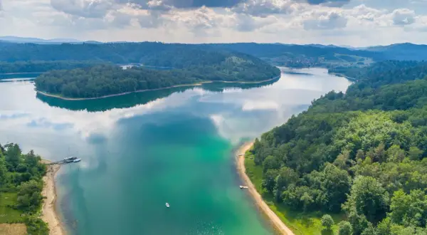 Malownicze jezioro w Polsce otoczone lasami, z łodziami przy brzegu i samotną żaglówką na wodzie. Idealne miejsce, gdzie nad jezioro w Polsce można uciec od zgiełku.