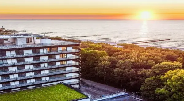 Idealny urlop nad morzem z wyżywieniem: nowoczesny hotel z widokiem na zachód słońca nad Bałtykiem, otoczony zielenią.