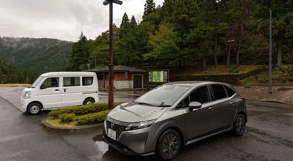 Szary Nissan i biały van na parkingu w Japonii. Widać, jaki ruch jest w Japonii, gdy podróżuje się po malowniczych terenach.