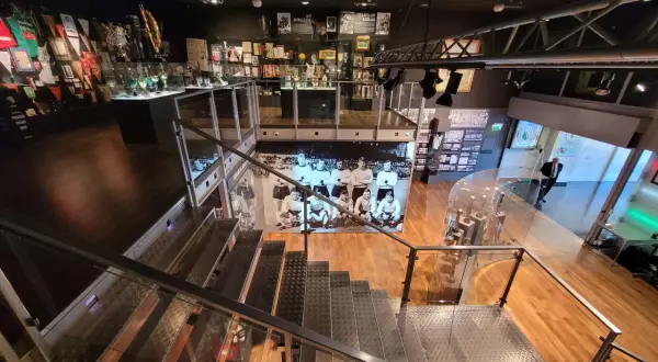 Wnętrze muzeum sportu w Warszawie. W gablotach pamiątki, puchary i zdjęcia. Schody prowadzą do kolejnych ekspozycji.