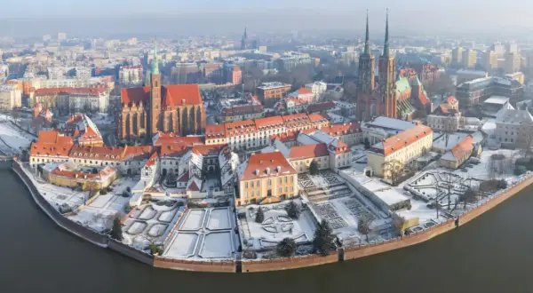 Wrocławskie atrakcje zimą: Ostrów Tumski pokryty śniegiem, z widokiem na katedrę i zabytkowe kamienice nad rzeką.
