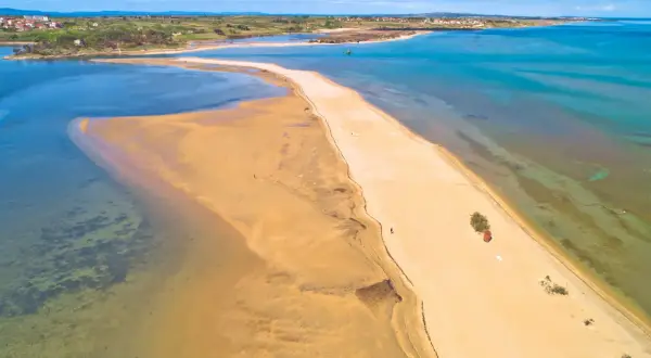 Piaszczyste plaże Chorwacji w całej okazałości. Długi, piaszczysty cypel otoczony turkusową wodą, z widokiem na miasteczko w oddali.