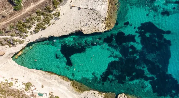 Malta plaże: turkusowa woda zatoki, skaliste wybrzeże i kilka osób kąpiących się w słońcu.