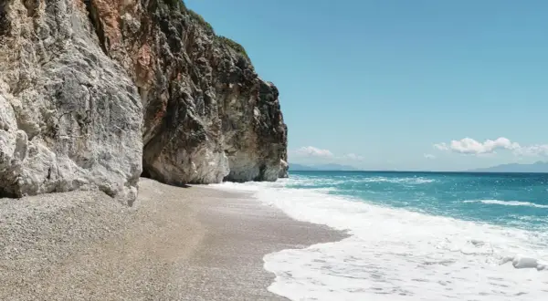 Skaliste klify otaczają kamienistą plażę Gjipe Beach, gdzie turkusowe morze łagodnie faluje.