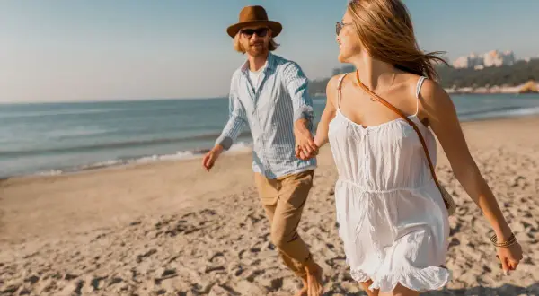 Szczęśliwa para podczas spaceru nad morzem. Trzymają się za ręce, biegnąc po piaszczystej plaży.