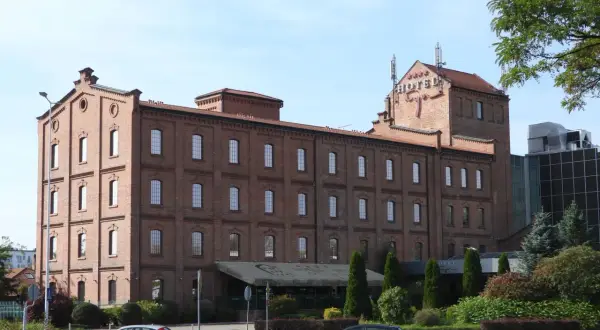 Hotel Młyn we Włocławku, ceglany budynek z czerwonym napisem HOTEL na dachu, otoczony zielenią.