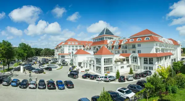 Elegancki hotel 5 gwiazdkowy nad morzem z przestronnym parkingiem pełnym samochodów.