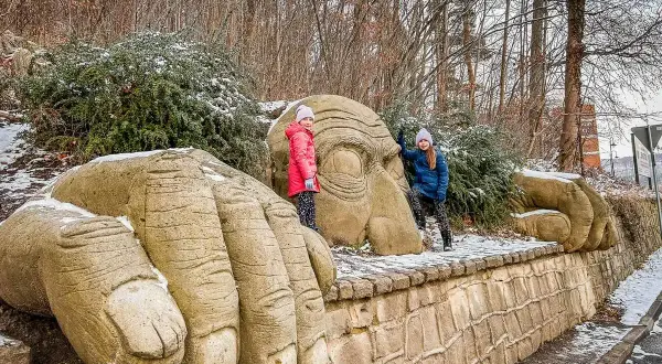 Dwie dziewczynki pozują przy gigantycznych kamiennych dłoniach i twarzy w Kudowie Zdrój. Góry w tle.