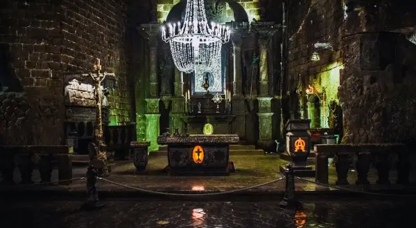 Wnętrze kaplicy w kopalniach soli w Wieliczce i Bochni. Kryształowy żyrandol oświetla ołtarz i kamienne rzeźby.