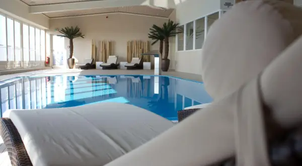 Relaks przy basenie w hotelu Radisson Blu Cottbus. Leżaki czekają na gości obok błękitnej wody i palm.
