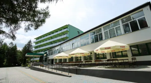 Zielony budynek sanatorium z balkonami i tarasem z parasolami Tyskie. Miejsce idealne dla szukających najlepszych sanatoriów w Polsce.