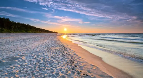 Zachód słońca nad morzem, piaszczysta plaża z odciskami stóp, las w tle. Idealne, fajne miejsce nad morzem dla dwojga na romantyczny spacer.