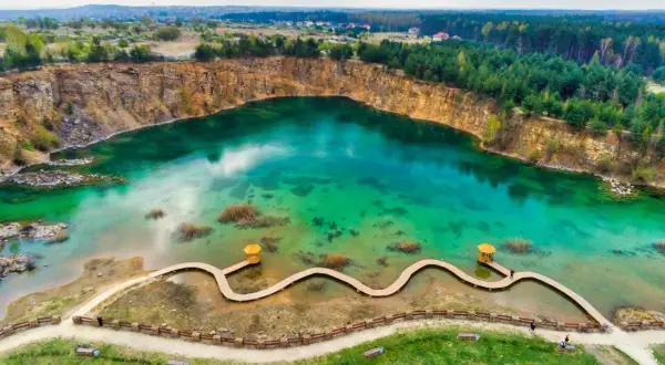 Turkusowe, magiczne jeziora w Polsce, dawny kamieniołom z drewnianą kładką i altanką, otoczony lasem i skalnymi zboczami.