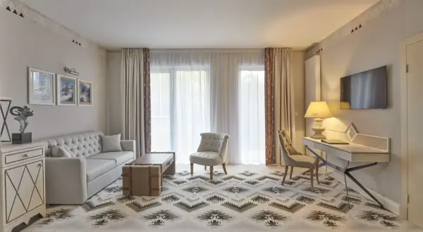 Elegancki salon w hotelu 5 gwiazdkowym. Sofa, stolik, fotele i biurko tworzą przytulną przestrzeń. Wzory na dywanie i zasłonach dodają charakteru.