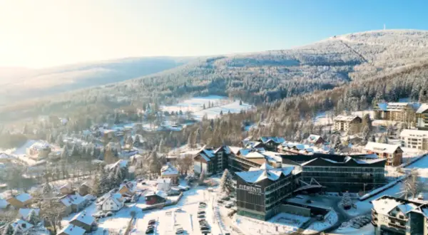Zimowy krajobraz z hotelem Elements, który oferuje idealny hotel ze stokiem. Wokół ośnieżone drzewa i góry.