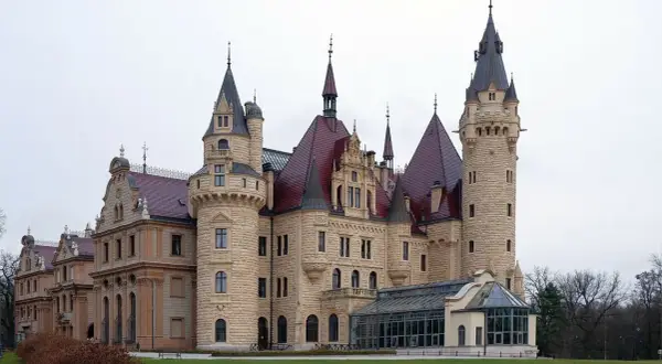 Kamienny zamek z czerwonymi dachami i wieżami, przypominający najstarsze zamki w Polsce.