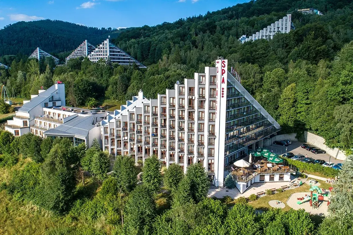 Hotel Diament Wisła w otoczeniu zieleni, z charakterystyczną architekturą schodkową i przeszklonymi fasadami.