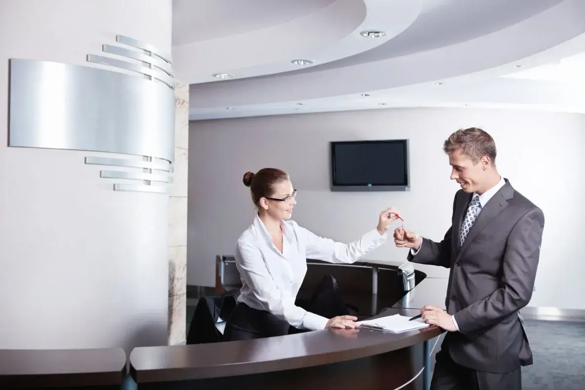 Miła technik hotelarstwa przekazuje klucze gościowi przy recepcji.