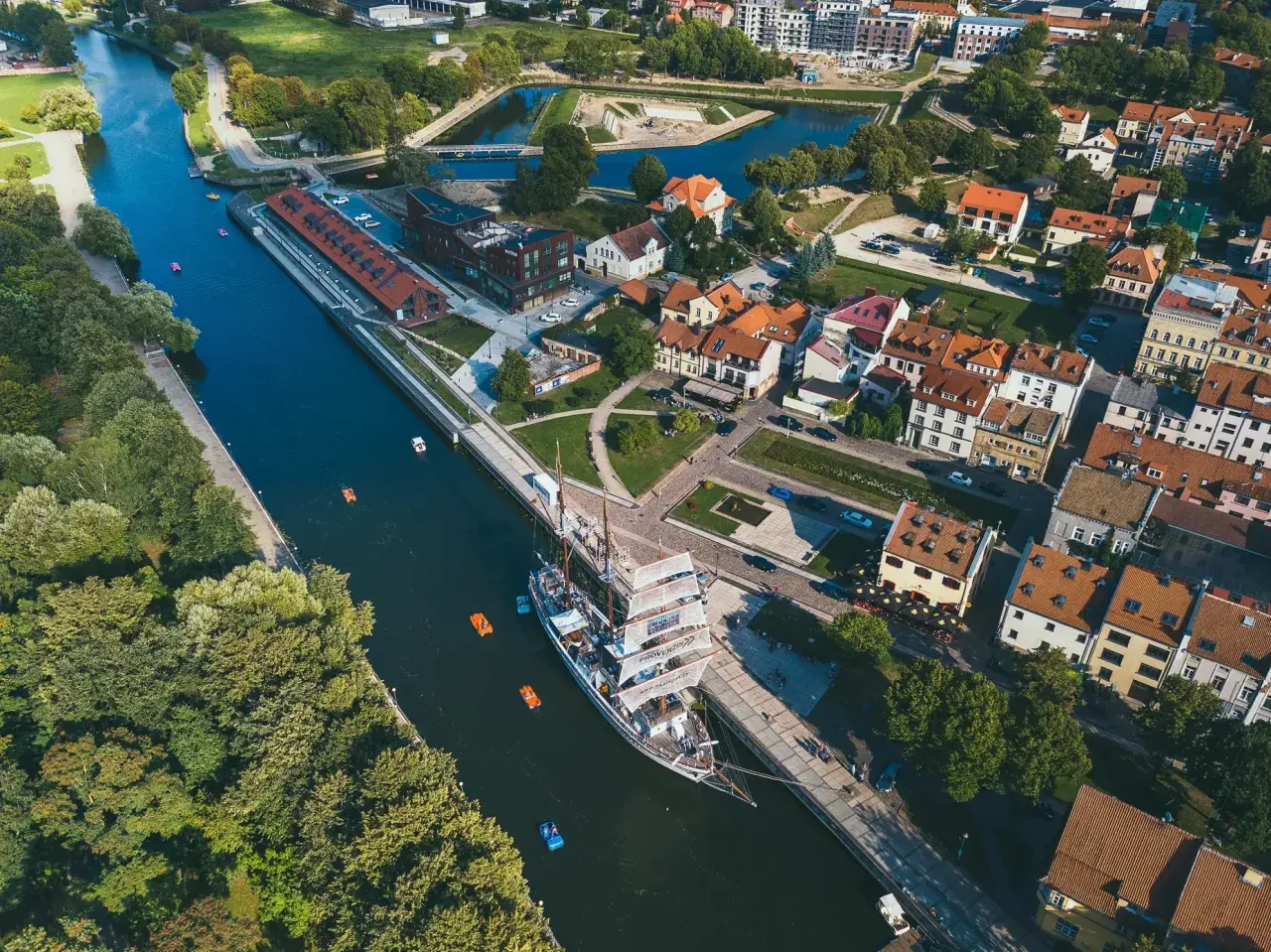 Widok z lotu ptaka na miasto na Litwie z kanałem, żaglowcem i kolorowymi łódkami.
