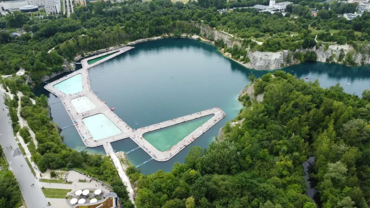 Wakacyjny wypoczynek nad wodą w Krakowie. Drewniane pomosty z basenami i leżakami otaczają turkusowe jezioro w otoczeniu zieleni.