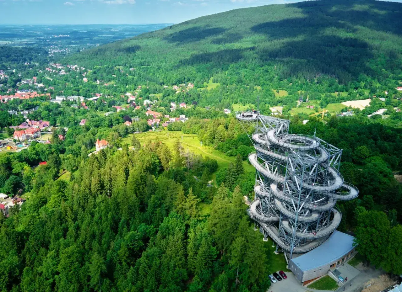 Widok na wieżę widokową w otoczeniu zielonych lasów i miasteczka. Idealne miejsce, gdzie w góry można wybrać się na spacer i podziwiać panoramę.