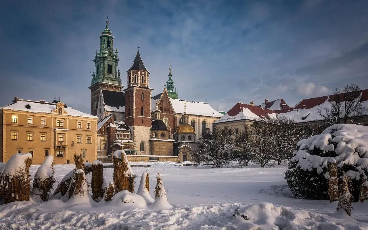 Zamek Królewski na Wawelu w zimowej scenerii. Pokryte śniegiem dachy i drzewa tworzą magiczny widok, idealny na kraków atrakcje zimą.