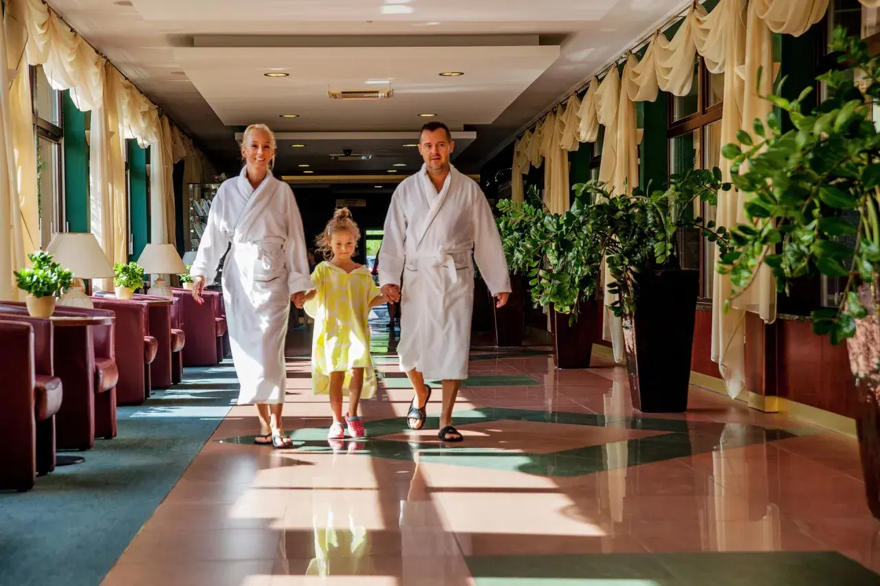 Rodzina w szlafrokach idzie korytarzem hotelowym. To idealne miejsce, by poczuć, co to jest spa i odpocząć.