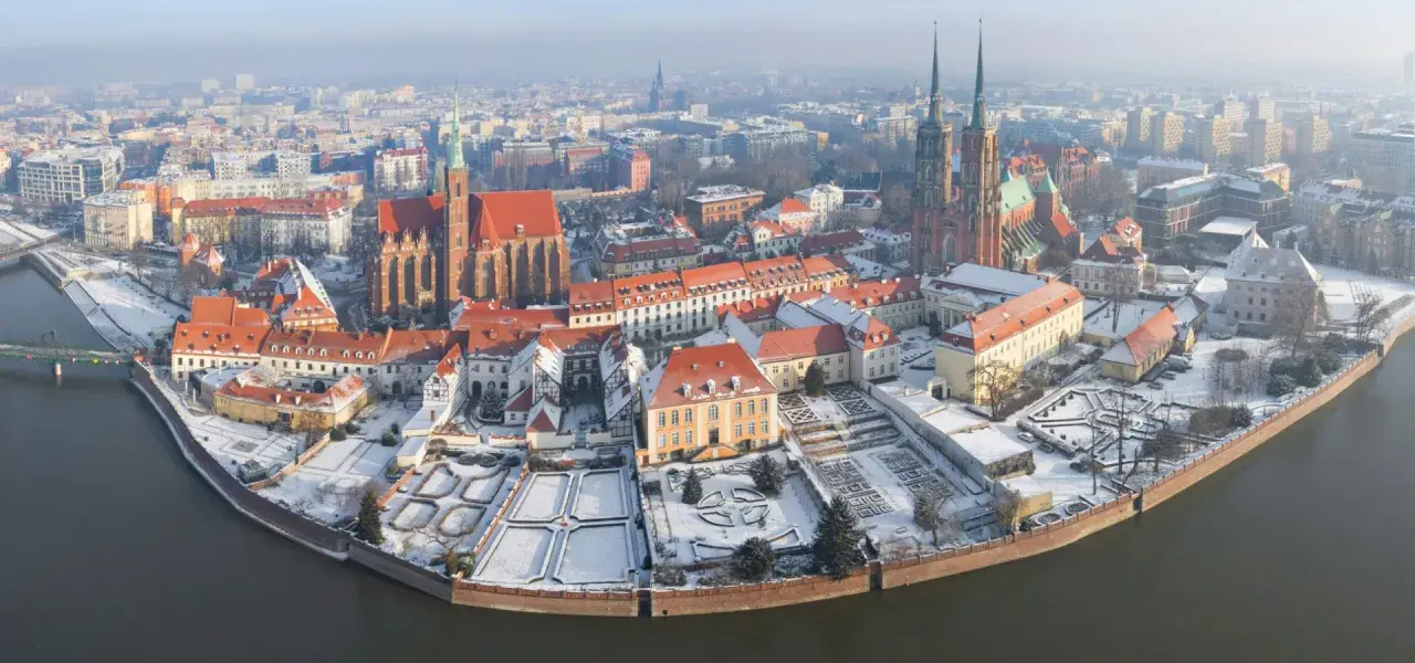 Wrocławskie atrakcje zimą: Ostrów Tumski pokryty śniegiem, z widokiem na katedrę i zabytkowe kamienice nad rzeką.