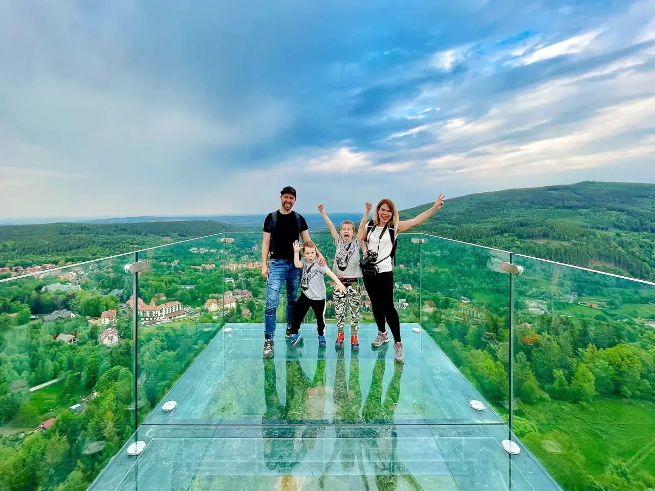 Rodzina na szklanym tarasie najwyższej wieży widokowej w Polsce. Zachwycający widok na zielone wzgórza i miasteczko.
