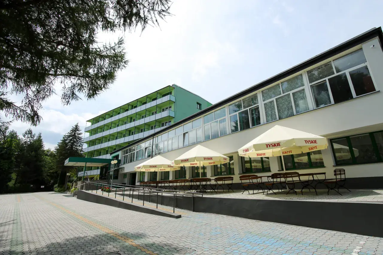 Zielony budynek sanatorium z balkonami i tarasem z parasolami Tyskie. Miejsce idealne dla szukających najlepszych sanatoriów w Polsce.