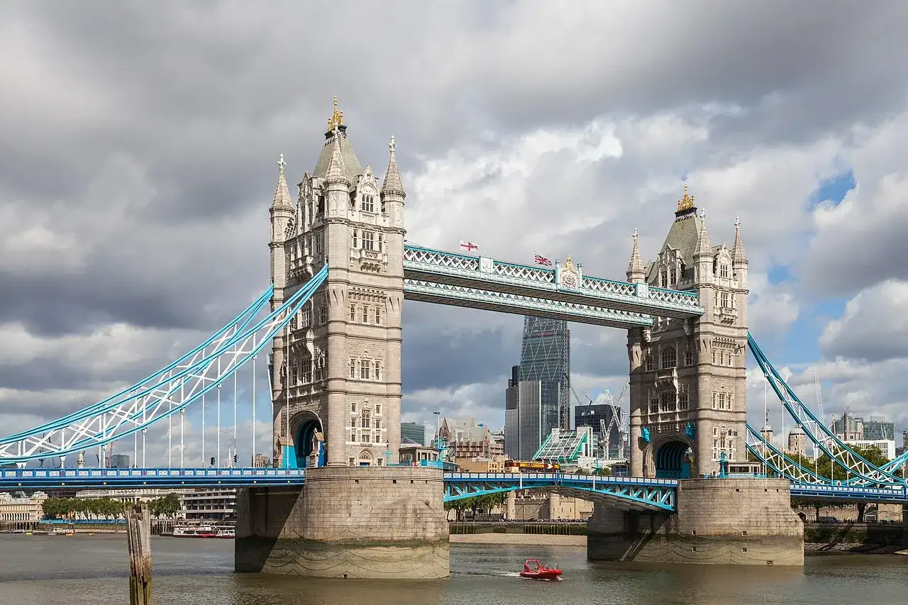 Słynny most w Wielkiej Brytanii, Tower Bridge, z charakterystycznymi wieżami i niebieskimi linami, na tle pochmurnego nieba.