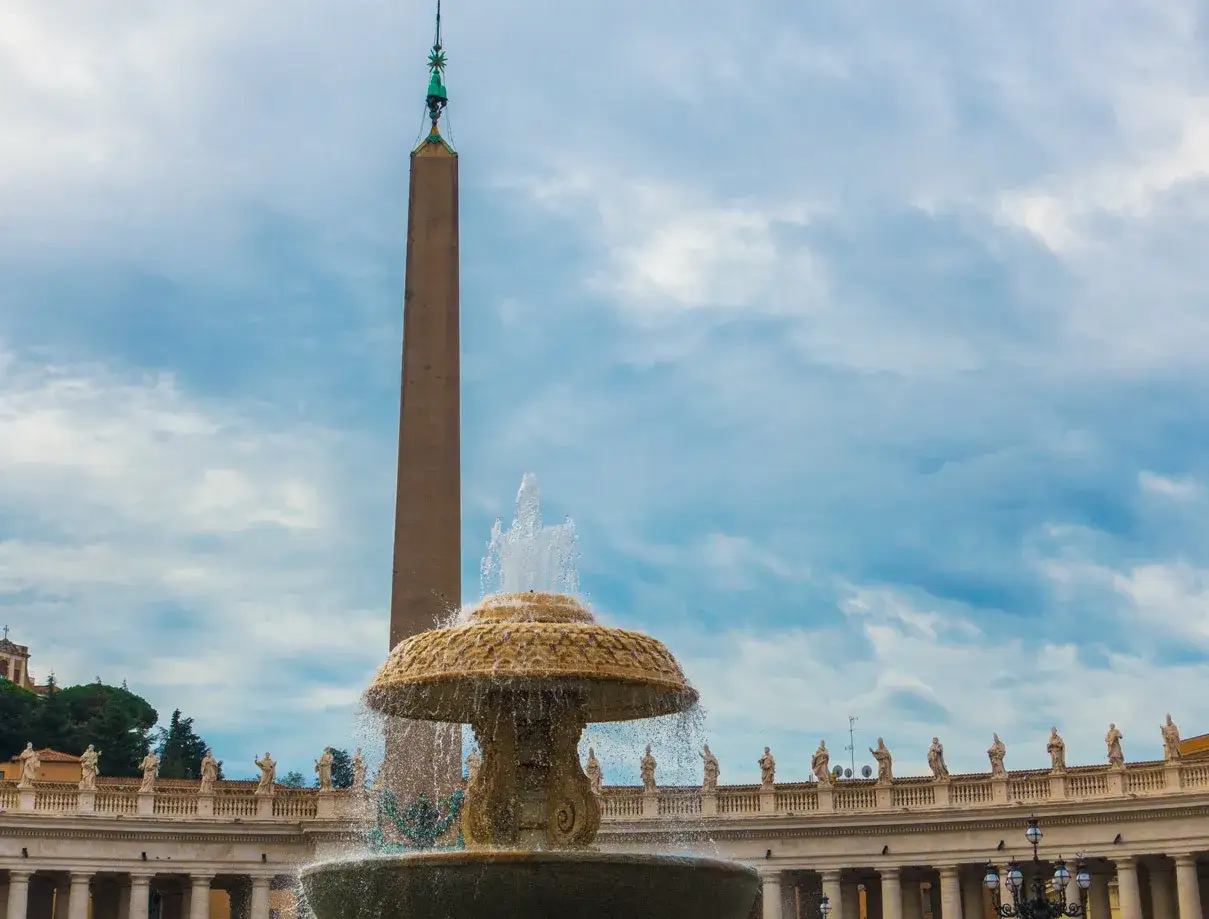 Fontanna i obelisk na placu św. Piotra w Rzymie. W tle kolumnada z posągami.