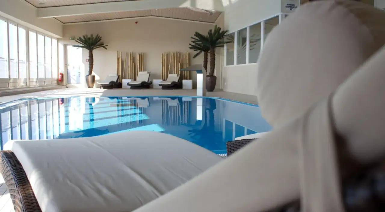 Relaks przy basenie w hotelu Radisson Blu Cottbus. Leżaki czekają na gości obok błękitnej wody i palm.
