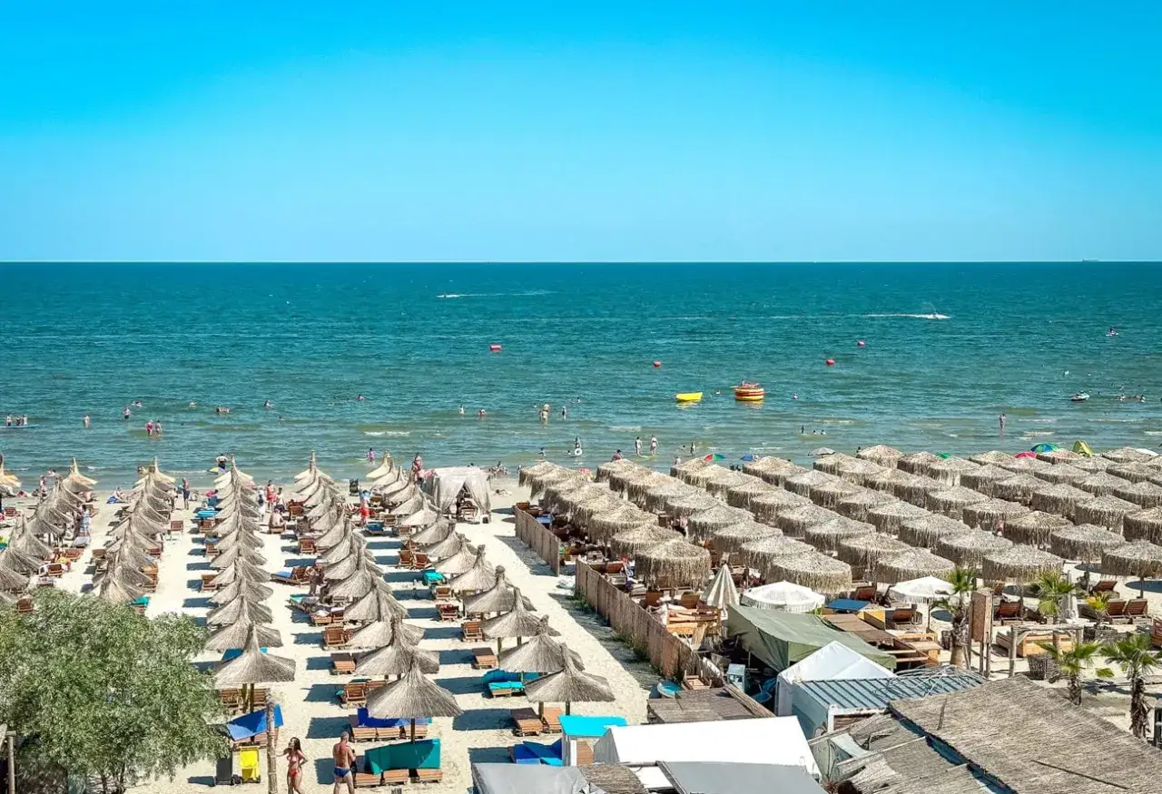 Słoneczna plaża w Rumunii, idealny klimat do wypoczynku nad Morzem Czarnym. Rzędy parasoli, ludzie kąpiący się w morzu.