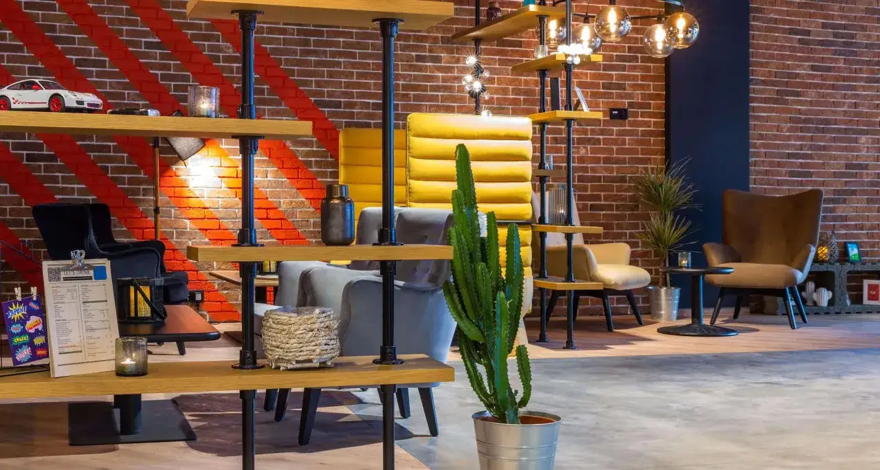 Nowoczesne wnętrze lobby hotelu Radisson Park Hotel Poznań z ceglaną ścianą, żółtymi i szarymi fotelami oraz regałami.