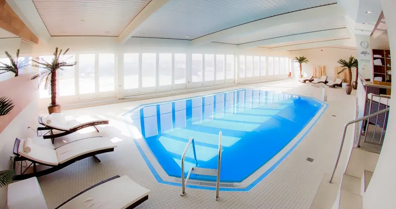 Basen w hotelu Radisson Blu Cottbus, z leżakami i palmami, zaprasza do relaksu.
