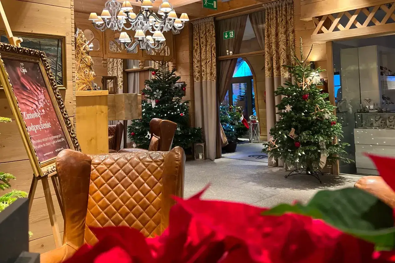 Przytulne wnętrze hotelu z choinkami i ozdobami, tworzące atmosferę świąt Bożego Narodzenia.