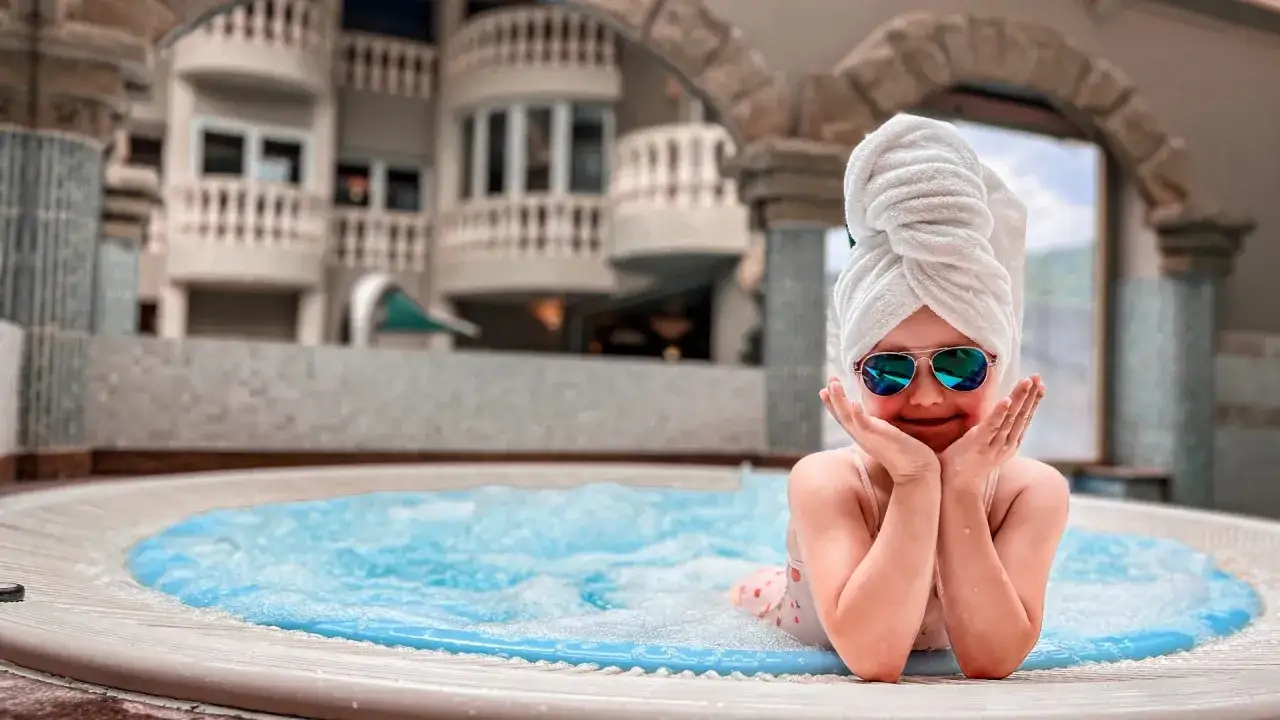 Mała dziewczynka w ręczniku i okularach przeciwsłonecznych w jacuzzi. Idealne miejsce, gdzie na wakacje z niemowlakiem, by odpocząć i zrelaksować się.