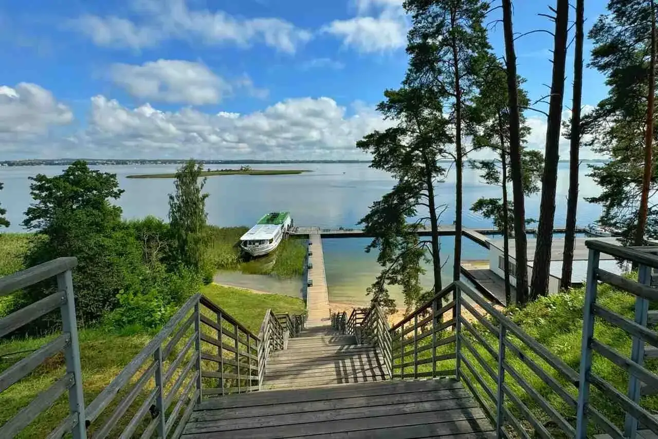 Malownicze mazury miejscowości nad jeziorem. Drewniane schody prowadzą do pomostu, przy którym cumuje statek.