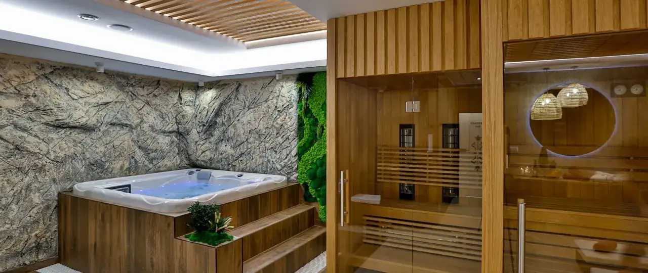 Relaks w nowoczesnym spa: jacuzzi z kamienną ścianą i zielonym mchem, obok drewniana sauna z przeszklonymi drzwiami.